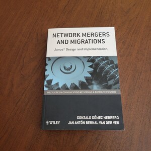 以下が含まれることがあります： 「Network Mergers and Migrations: Junos Design and Implementation」というタイトルのソフトカバー本。表紙は、黒い文字が書かれた白い上部、中央の金属製ギアの画像、そして著者名が記載された黒い下部で構成されています。