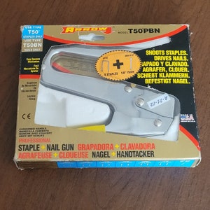 Puede incluir: Una grapadora de metal plateada con mango amarillo. El empaque dice "T50PBN" y "Grapadora + Clavadora Profesional".