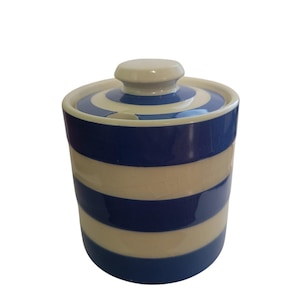 May include: A cylindrical ceramic jar with a lid, featuring horizontal stripes in deep blue and off-white. The lid has a central knob and a small notch for a spoon. The off-white sections of the ceramic body show a fine, visible crackle glaze finish.