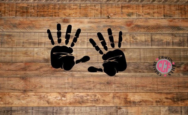 May include: Two black handprints on a wooden background. The handprints are side by side and are facing the viewer. The handprints are a simple silhouette with no details.