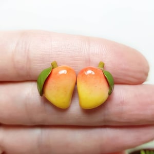May include: A pair of mango-shaped earrings with green leaves. The earrings are made of polymer clay and are painted in shades of yellow, orange, and red.