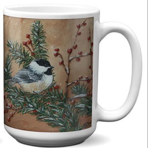 May include: White ceramic mug featuring a detailed painting of a chickadee bird perched on a pine branch with red berries. The artwork is set against a brown background, with a touch of snow. The mug has a large handle.