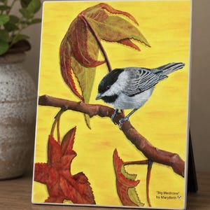 May include: A rectangular art print featuring a black-capped chickadee perched on a brown branch against a bright yellow background. Red and green maple leaves surround the bird. The text "Big Medicine" by MaryBeth is printed in the corner.