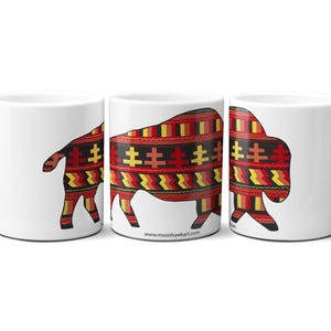 May include: White ceramic mugs featuring a bison design. The bison silhouette is filled with a colourful pattern of red, yellow, and black geometric shapes. The mugs are displayed in a row, showcasing the design from different angles.