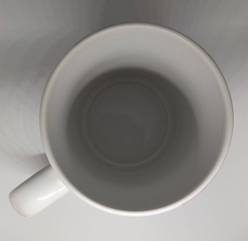 May include: A white ceramic mug with a rounded interior and a handle on the side. The mug is empty and sits on a white surface. The mug's interior is a darker shade of gray.