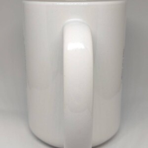 May include: A white ceramic mug with a curved handle. The mug has a glossy finish and a simple, clean design. The handle is thick and rounded, providing a comfortable grip. The mug is suitable for hot or cold beverages.