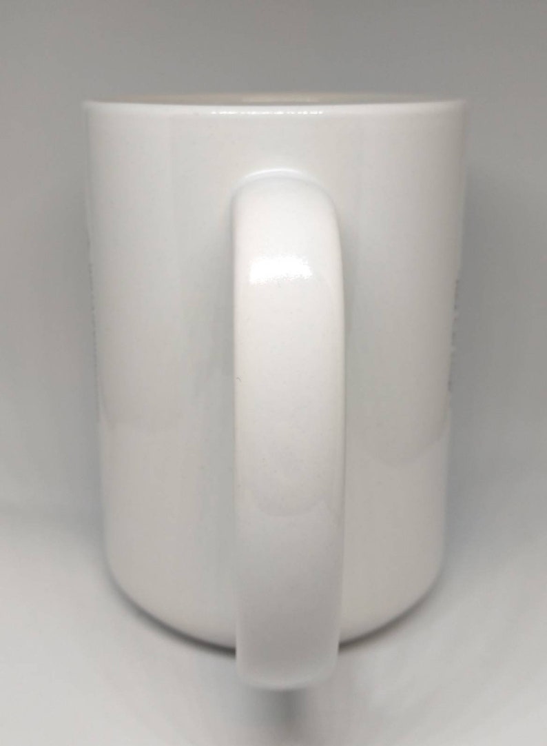 May include: A white ceramic mug with a curved handle. The mug has a glossy finish and a simple, clean design. The handle is thick and rounded, providing a comfortable grip. The mug is suitable for hot or cold beverages.