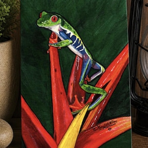 May include: A rectangular canvas painting featuring a vibrant red-eyed tree frog with green, blue, and yellow markings perched on bright red and yellow tropical flower petals against a dark green background. The artist's signature is visible.