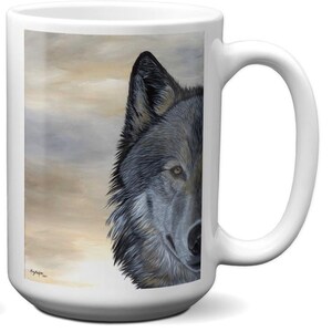 May include: White ceramic mug featuring a detailed painting of a wolf's face. The wolf's fur is shades of gray and black, with a piercing yellow eye. The background is a soft blend of beige and gray, creating a serene atmosphere.