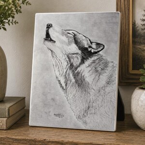 May include: A rectangular plaque featuring a detailed graphite pencil drawing of a wolf howling with its head tilted upward. The artwork is rendered in shades of gray and black on a light background, capturing the texture of the fur and facial features.