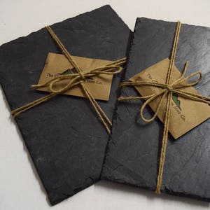 May include: Two black slate serving trays tied together with twine and brown paper gift tags. The tags have the text "The Original Slate Co."