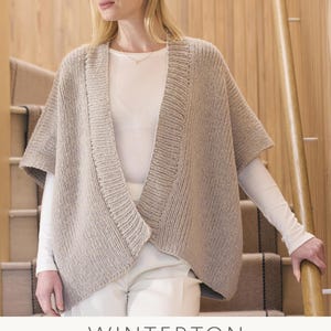 May include: A woman wearing a beige knitted cardigan with a V-neck and short sleeves. The cardigan is called "Winterton" and is designed by Quail Studio. The yarn used is Merino Soft and Alpaca Haze. The image is from Mode at Rowan.