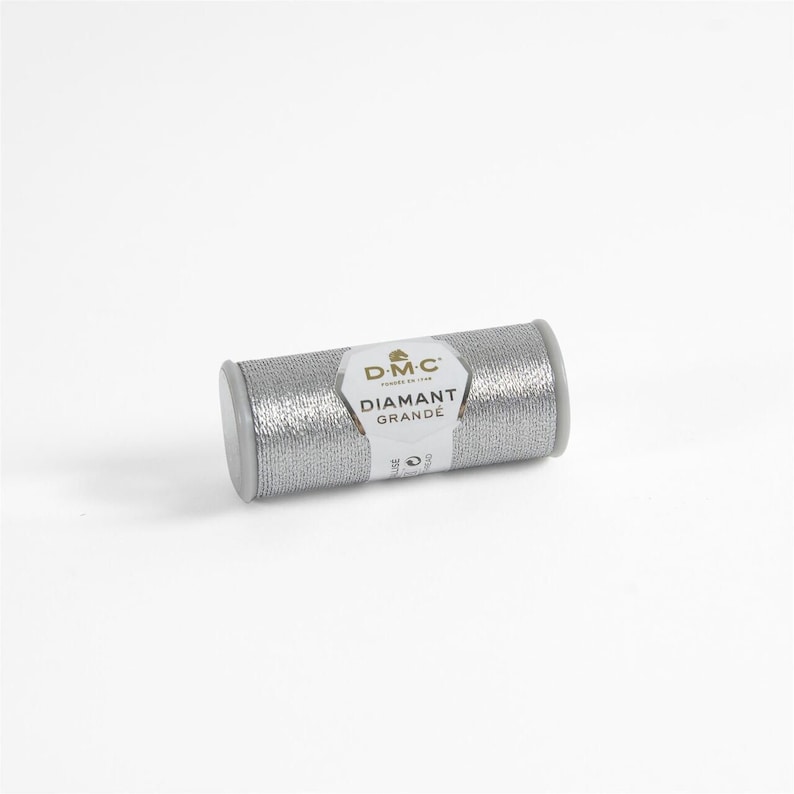 May include: A silver spool of DMC Diamant Grande embroidery thread. The spool has a white label with the DMC logo and the text "Diamant Grande".