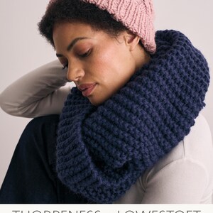May include: A pink knitted hat with a pom pom on top and a navy blue knitted infinity scarf. The hat and scarf are designed by Quail Studio and are made with chunky wool. The text "MODE at ROWAN" is visible in the top right corner of the image.