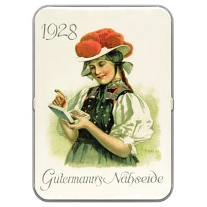 May include: A vintage tin box featuring a woman in a red and white hat holding a small box. The text on the box reads "Gütermann's Nähseide" and "1928".