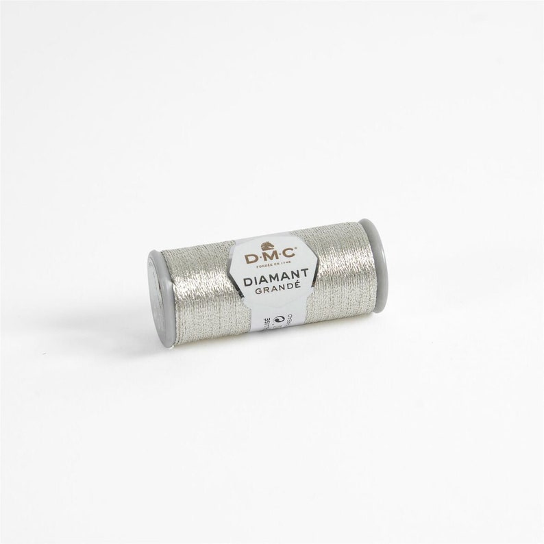May include: A silver spool of DMC Diamant Grande embroidery thread. The spool is labeled with the DMC logo and the text "Diamant Grande".