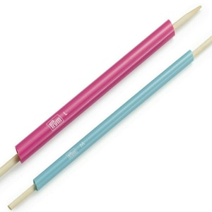 May include: Two wooden knitting needles with pink and blue plastic tips. The pink needle is labeled "Prym L" and the blue needle is labeled "Prym M".