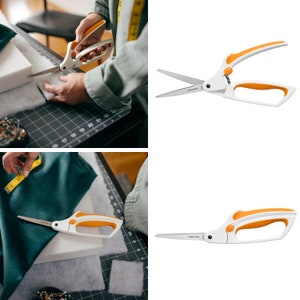 May include: A pair of Fiskars fabric shears with orange handles. The shears are shown cutting fabric on a cutting mat.