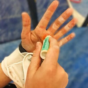 May include: A person is applying a green and white tube of hand cream to their hand. The hand is red and has white chalk on it.