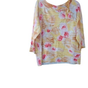 Peut inclure: Un chemisier &agrave; manches trois-quarts avec un motif floral. Le chemisier pr&eacute;sente un fond jaune avec des motifs floraux roses et marron. Le col a un design asym&eacute;trique.