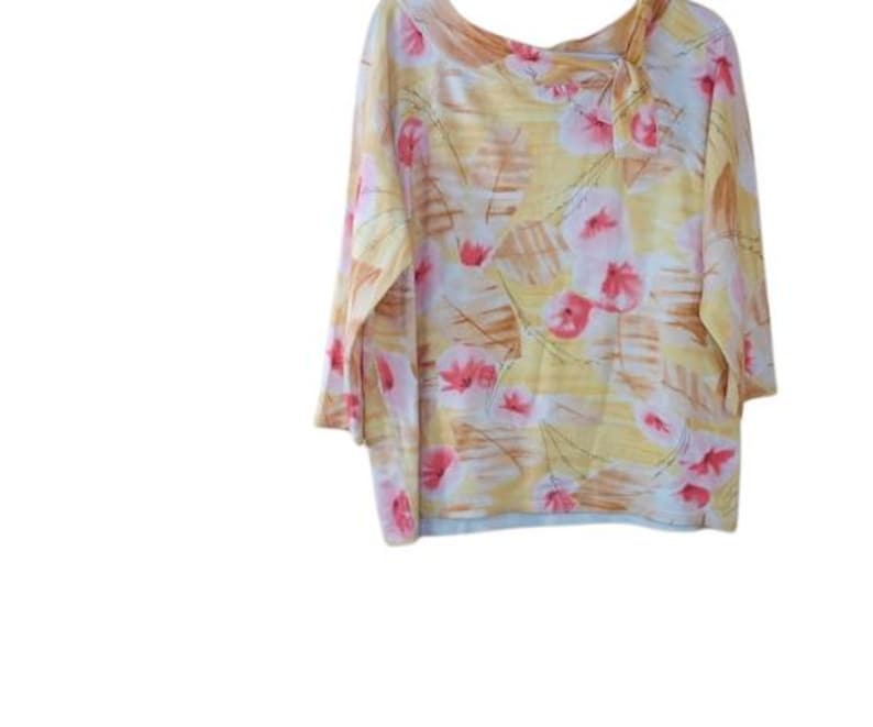 Peut inclure: Un chemisier &agrave; manches trois-quarts avec un motif floral. Le chemisier pr&eacute;sente un fond jaune avec des motifs floraux roses et marron. Le col a un design asym&eacute;trique.