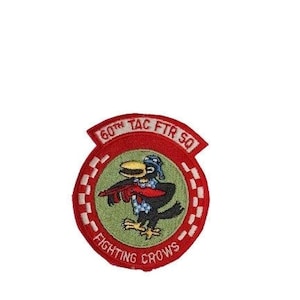 May include: An embroidered patch in red, white and green with the text "60th TAC FTR SQ FIGHTING CROWS" and a cartoon crow holding a red object.