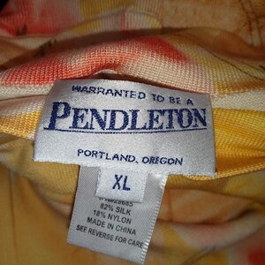 Peut inclure: Gros plan sur une &eacute;tiquette Pendleton avec le texte "WARRANTED TO BE A PENDLETON PORTLAND, OREGON XL 82% SILK 18% NYLON MADE IN CHINA SEE REVERSE FOR CARE." Le tissu pr&eacute;sente un motif floral jaune, orange et rouge.