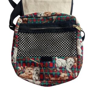 May include: A crossbody bag with a flap and adjustable strap. The bag features a red, green, and black plaid pattern with images of dogs. It has a black mesh pocket and a zippered compartment.