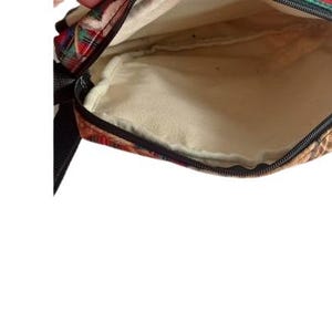 May include: Open view of a small, rectangular bag with a plaid pattern in red, green, and gold. The interior is a light beige color. A black strap is visible on the left side, and a zipper runs along the top edge.