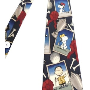May include: A blue necktie with a repeating pattern of Snoopy playing golf, golf clubs, golf balls, and trophies. The tie has a red, white, and blue color scheme.