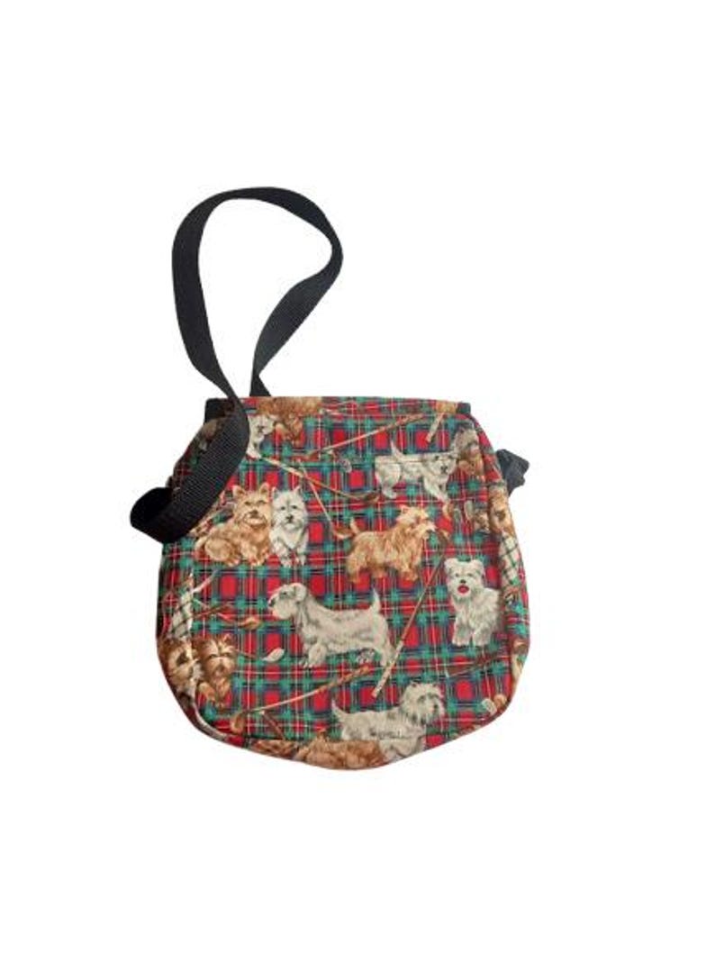 May include: A small, round bag with a black handle. The bag features a red and green plaid pattern with various dog breeds printed on it. The bag is made of fabric and has a simple design.