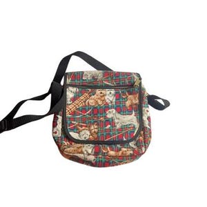 May include: A square, patterned shoulder bag with a black strap. The bag features a red and green plaid design with various dog breeds printed across the fabric. The bag has a zipper closure.