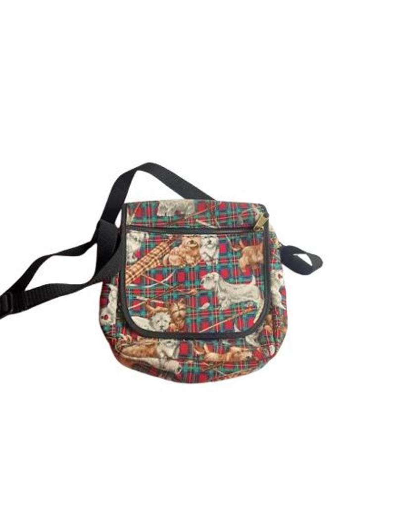 May include: A square, patterned shoulder bag with a black strap. The bag features a red and green plaid design with various dog breeds printed across the fabric. The bag has a zipper closure.