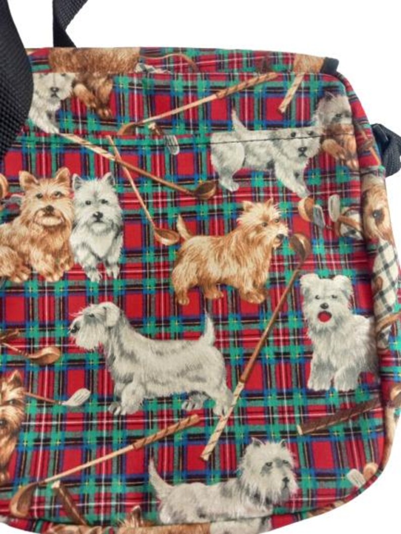 May include: A square bag with a red, green, and blue plaid pattern. The pattern is filled with illustrations of dogs and golf clubs. The bag has a black strap.