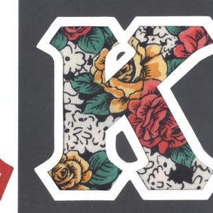 May include: Two large, red and white felt letters, A and K, with a floral pattern. The letters are outlined in white and have a vintage style.