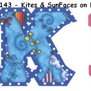 May include: Two fabric letters, K and E, with a blue sky background with white polka dots, kites, and sun faces. The letter K is outlined in blue and the letter E is outlined in pink.