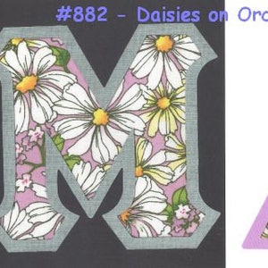 May include: Two fabric letters, M and A, with a daisy and orchid print. The letters are cut out of a light purple fabric with a white background. The letters are outlined in gray. The letters are on a black background. #882 - Daisies on Orchid