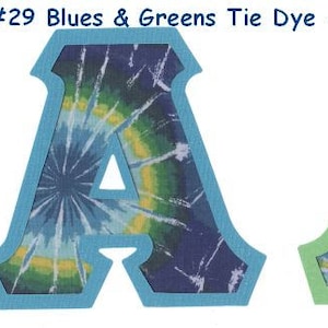 May include: Two tie-dye fabric letters, both in the shape of the letter "A". The letter on the left is outlined in blue and has a blue, green, and yellow tie-dye pattern. The letter on the right is outlined in green and has a green, blue, and yellow tie-dye pattern. #29 Blues & Greens Tie Dye - Limited Supply!