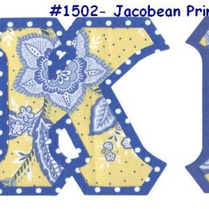 May include: Two fabric letters, K and M, in a blue and white floral pattern on a yellow background with white polka dots. The letters have a blue outline.