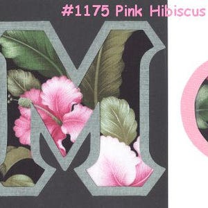 May include: Two fabric letters, an "M" and a "Phi", with a pink hibiscus floral pattern on a black background. The letters are outlined in gray.