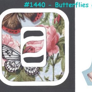 Puede incluir: Dos parches para planchar con fondo azul y contorno blanco. Los parches presentan un patrón de mariposas y rosas. El primer parche es un cuadrado con la letra "E" en el centro. El segundo parche tiene la forma de la letra "A". Ambos parches tienen el texto "#1440 - Mariposas y Rosas".