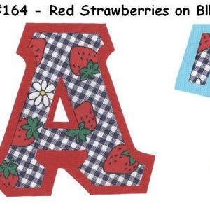 May include: Two fabric letters, A and T, in red and blue, with a gingham pattern and strawberry print. The letters are cut out and have a white background.