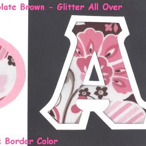 Puede incluir: Dos letras de tela, "A" y "O", con un patrón floral rosa y marrón. Las letras están delineadas en blanco y tienen un acabado brillante. El texto "#538 Pinks & Chocolate Brown - Glitter All Over" está por encima de las letras. El texto "UPick Border Color" está por debajo de las letras.