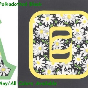 May include: A green outlined letter A with a black background and white daisies with yellow centers. The letter A is surrounded by a border of white daisies with yellow centers on a black background. The text #1620 Daisies on Polkadot Black is at the top of the image. The text U-Pick Border - Any/All Colors Available is at the bottom of the image.
