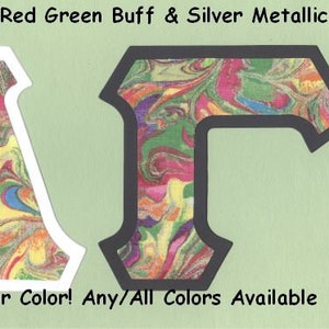 May include: Two large letters, "A" and "T", are made of a marbled red, green, and yellow fabric. The letters have a white and black border, respectively. The text "#1575 Marbled Red Green Buff & Silver Metallic" is at the top of the image. The text "U-Pick Border Color! Any/All Colors Available" is at the bottom of the image.