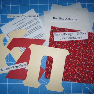 May include: A craft kit for making Greek letter templates. The kit includes fabric, bonding adhesive, and instructions. The fabric is red with white flowers. The letters are cut out of cream-colored paper.