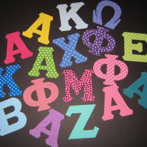 May include: A collection of felt letters in various colors and polka dot patterns. The letters include A, K,  Φ, Ω, E, M, Z, and B.