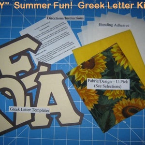 May include: A DIY craft kit for making Greek letters. The kit includes fabric, bonding adhesive, and templates for the letters. The fabric features a sunflower pattern on a green background. The letters are cut out of cream-colored cardstock.