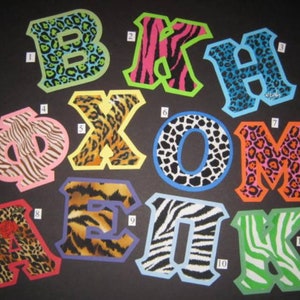 May include: Eleven colorful felt letters with animal print designs. The letters spell out "B X O M A E K".