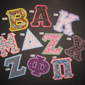 May include: A set of fabric letters in various colors and patterns, including pink, blue, yellow, green, and purple. The letters spell out "BAZMPX", with each letter having a unique design.